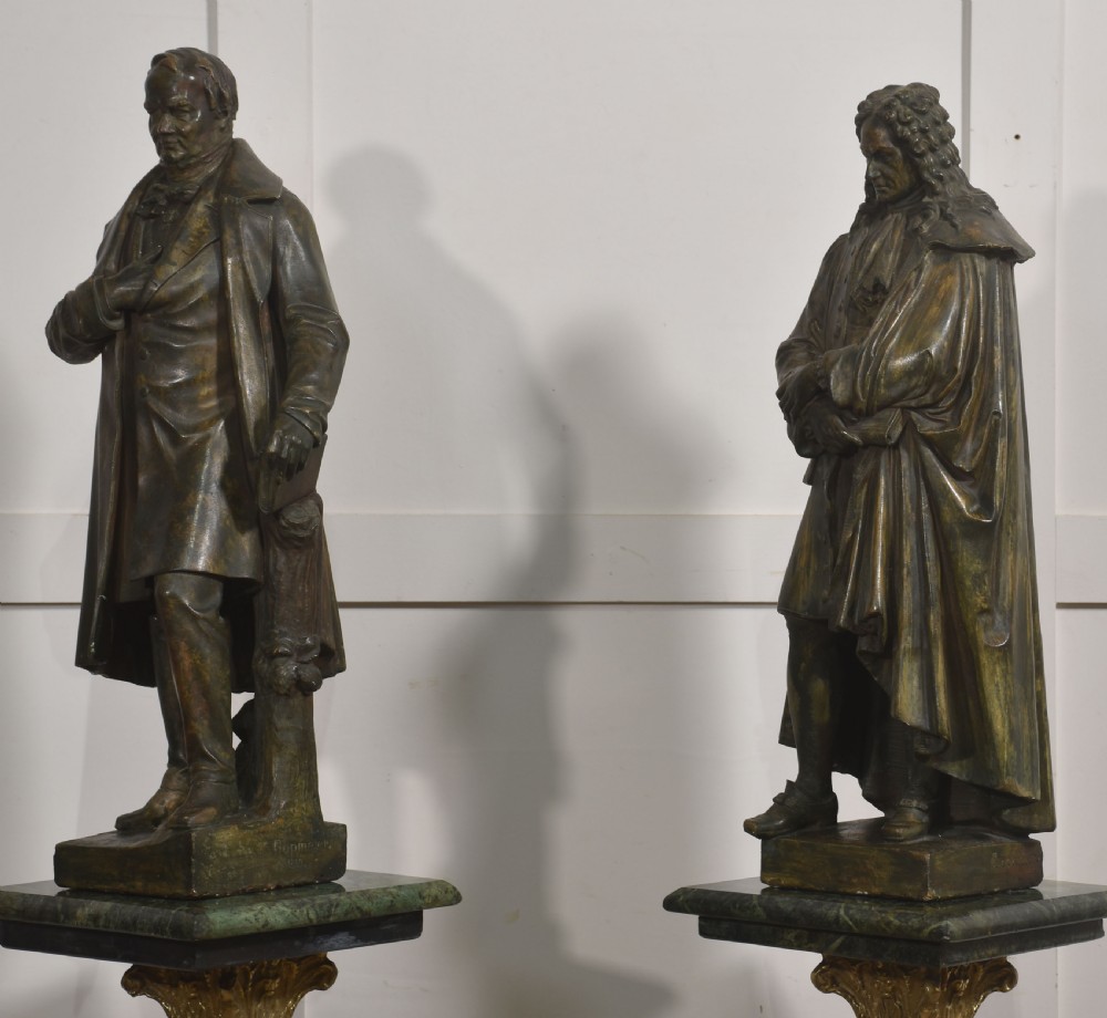 A pair of late nineteenth-century patinated chalkware statues depicting two standing male figures in historical attire on integral rectangular bases. View X