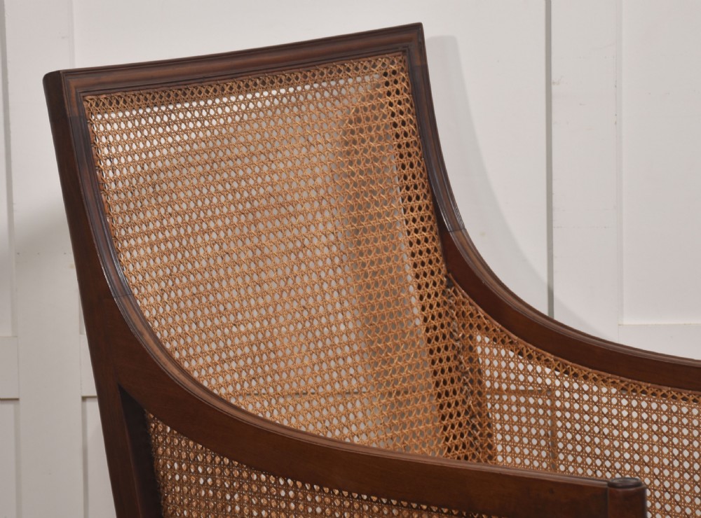 A Regency mahogany bergere armchair featuring woven cane back and side panels, turned front legs on brass castors, and light striped fabric cushions. View IX
