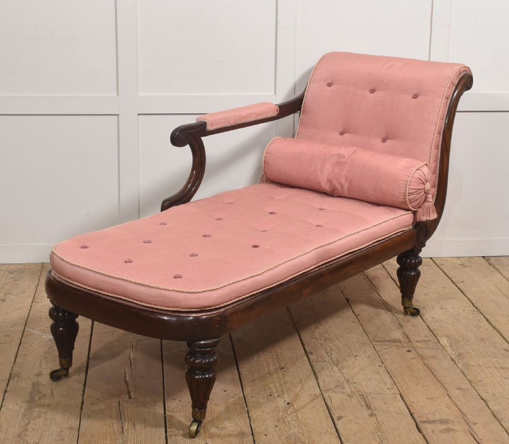 A William IV rosewood chaise longue upholstered in pink fabric with a matching bolster cushion and turned legs on brass castors.