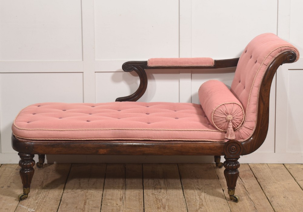 A William IV rosewood chaise longue upholstered in pink fabric with a matching bolster cushion and turned legs on brass castors. View IV