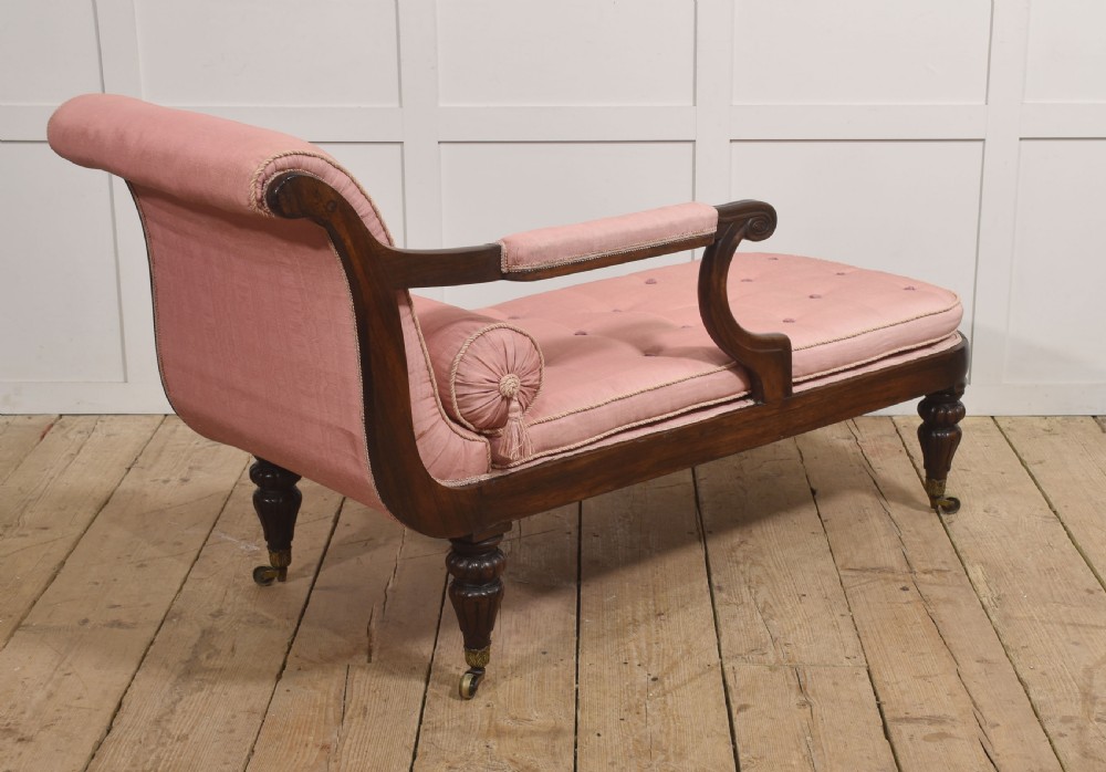 A William IV rosewood chaise longue upholstered in pink fabric with a matching bolster cushion and turned legs on brass castors. View XI