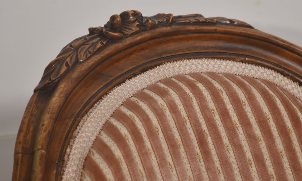 A carved walnut open armchair featuring an oval upholstered backrest in striped pink velvet, padded seat, and cabriole front legs with castors. View IV