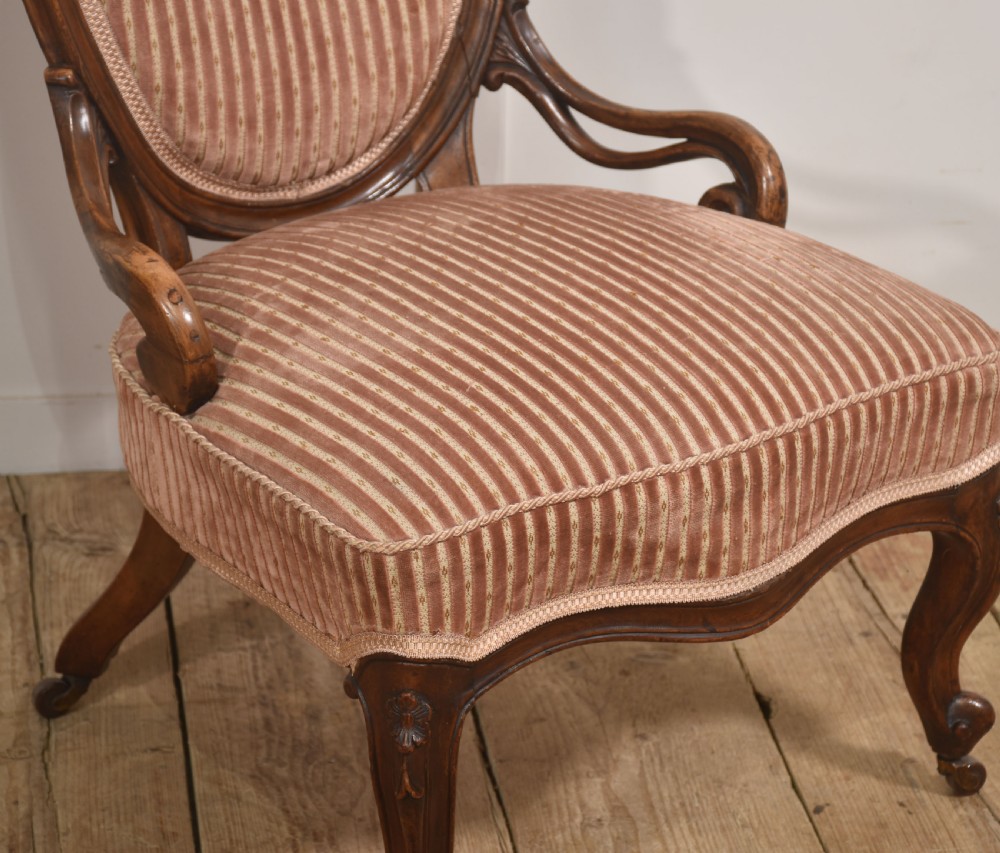 A carved walnut open armchair featuring an oval upholstered backrest in striped pink velvet, padded seat, and cabriole front legs with castors. View VI