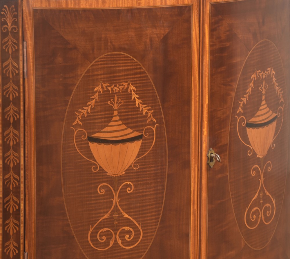 A floor-standing Sheraton Revival bow-front mahogany corner cabinet with satinwood neoclassical urn marquetry on twin doors. View IV