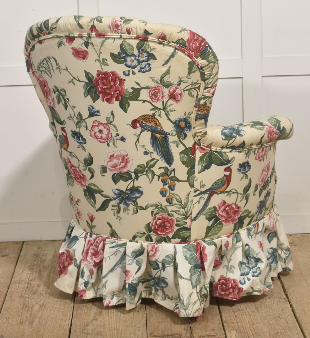 A late nineteenth-century Victorian armchair upholstered in cream floral and bird patterned fabric featuring a button-backed backrest and a pleated bottom skirt. View V