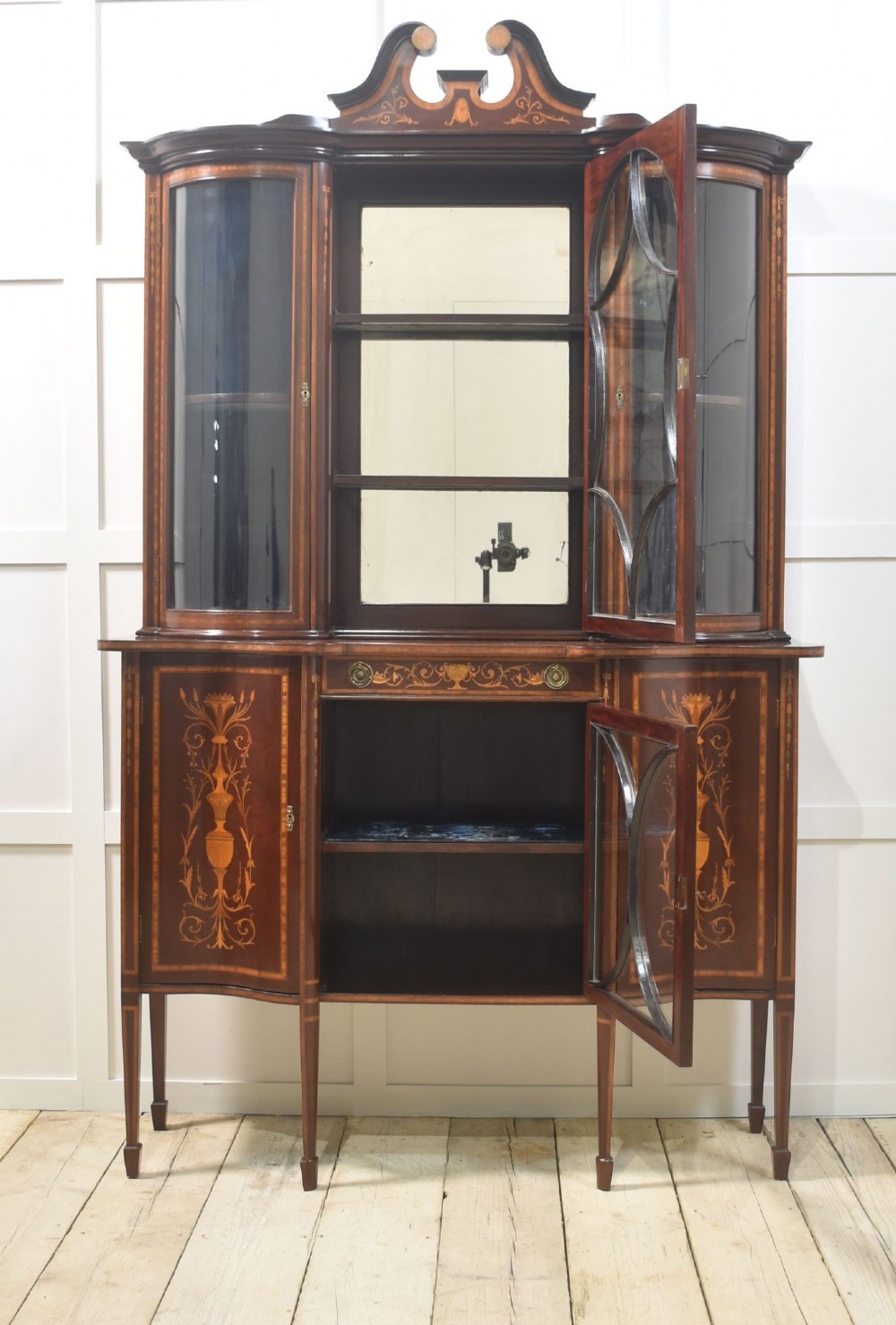 An Edwardian mahogany display cabinet featuring satinwood marquetry inlay, urn motifs, a swan-neck pediment, curved glass doors, and tapered legs. View VII