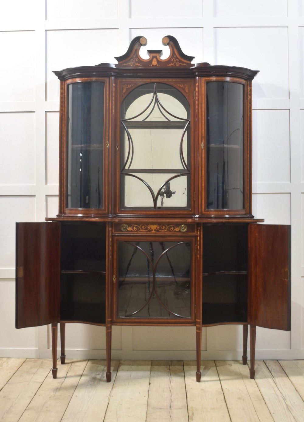 An Edwardian mahogany display cabinet featuring satinwood marquetry inlay, urn motifs, a swan-neck pediment, curved glass doors, and tapered legs. View VIII