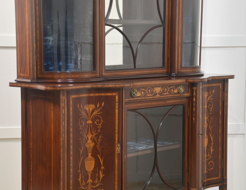 An Edwardian mahogany display cabinet featuring satinwood marquetry inlay, urn motifs, a swan-neck pediment, curved glass doors, and tapered legs. View XIII