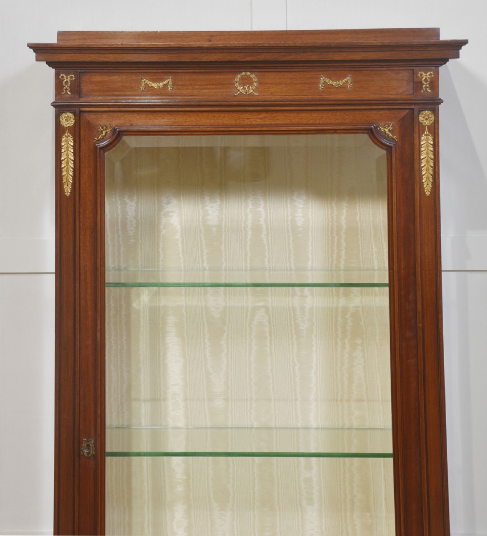 A tall Louis XVI style mahogany vitrine with a single glazed door, glass shelves, fabric-lined interior, and ornate metal mounts. View X