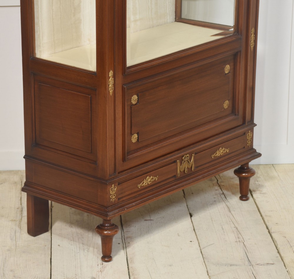 A tall Louis XVI style mahogany vitrine with a single glazed door, glass shelves, fabric-lined interior, and ornate metal mounts. View XI