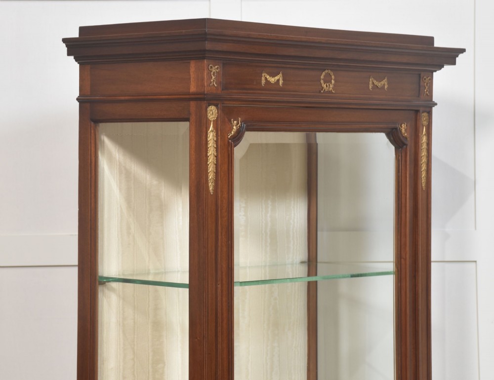 A tall Louis XVI style mahogany vitrine with a single glazed door, glass shelves, fabric-lined interior, and ornate metal mounts. View XII