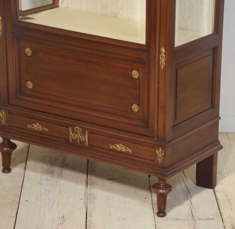 A tall Louis XVI style mahogany vitrine with a single glazed door, glass shelves, fabric-lined interior, and ornate metal mounts. View XIII