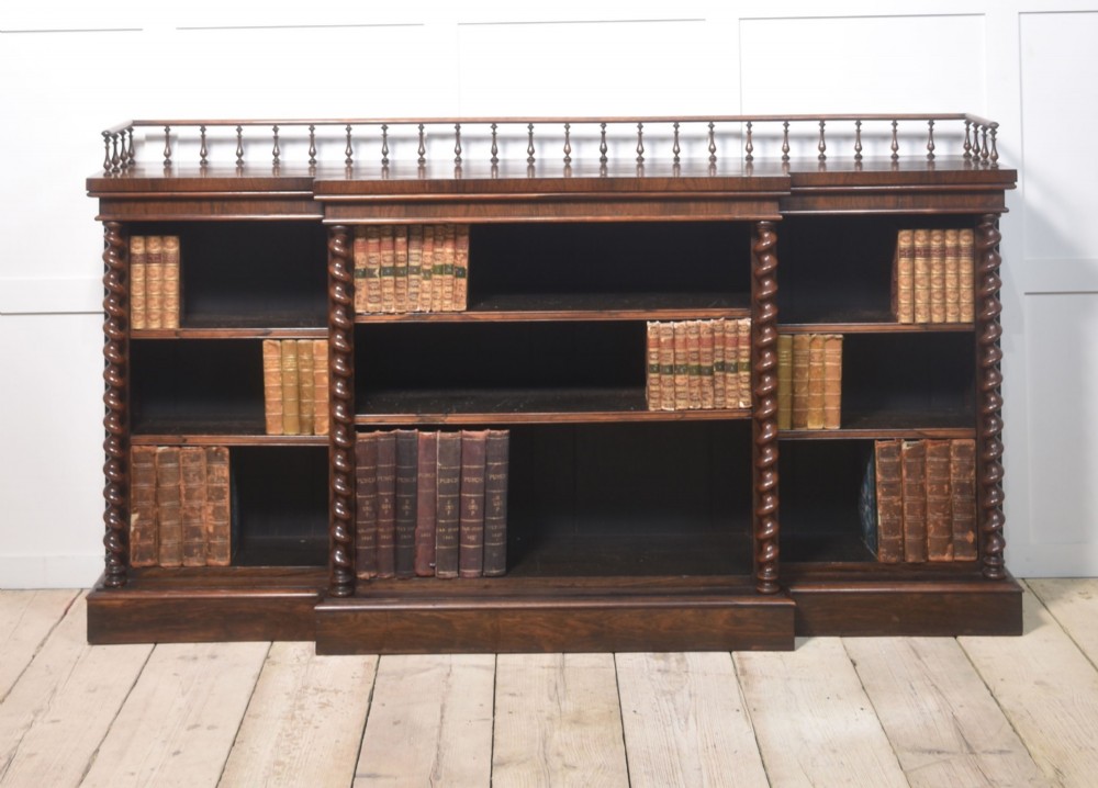 A large Victorian rosewood breakfront open bookcase featuring three shelf sections, carved barley twist columns, and a spindle gallery along the top edge.