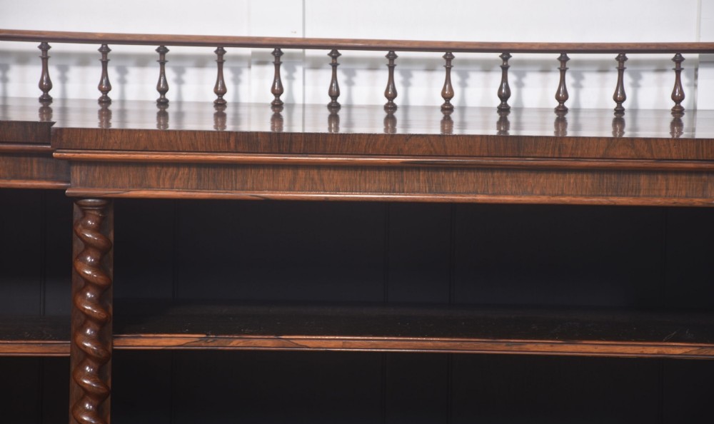 A large Victorian rosewood breakfront open bookcase featuring three shelf sections, carved barley twist columns, and a spindle gallery along the top edge. View IV