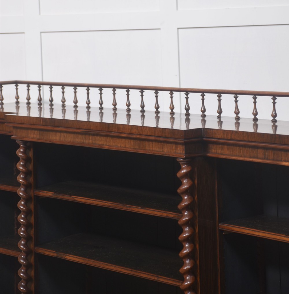 A large Victorian rosewood breakfront open bookcase featuring three shelf sections, carved barley twist columns, and a spindle gallery along the top edge. View X
