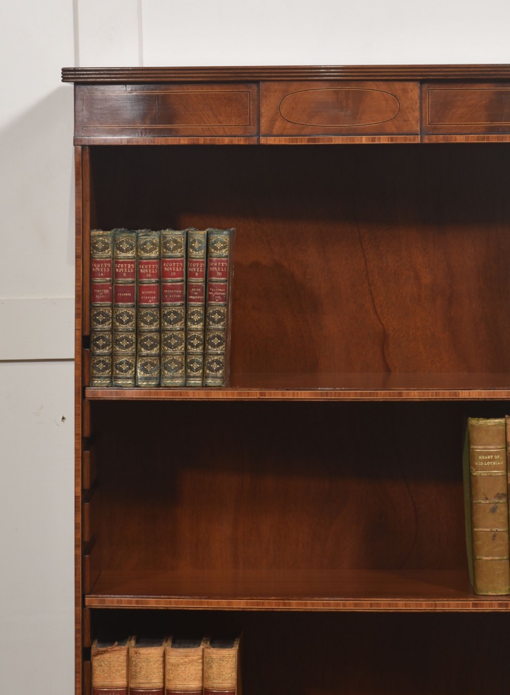 A tall, narrow mahogany open bookcase featuring five shelves, decorative inlay on the top frieze, and shaped bracket feet. View II