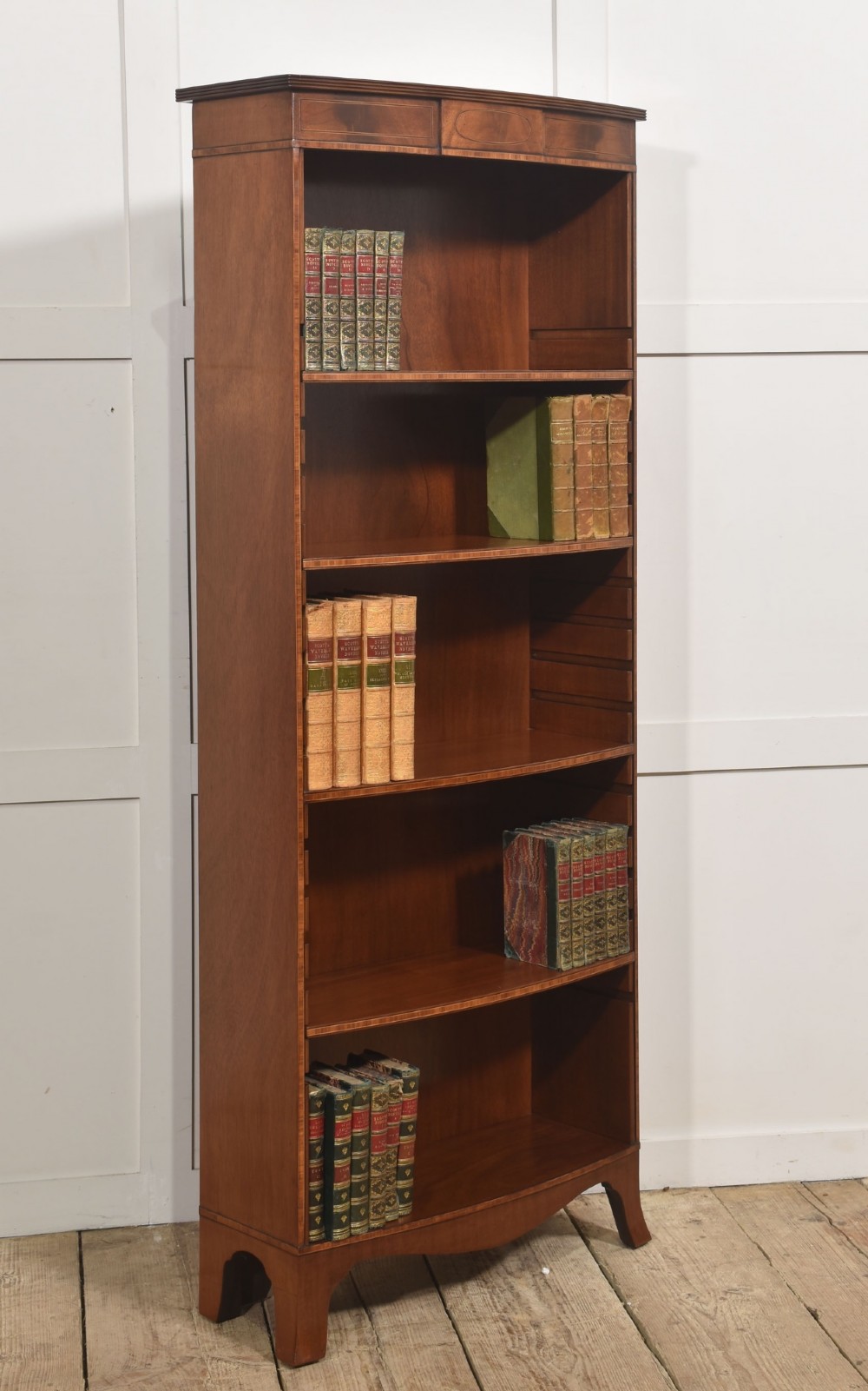 A tall, narrow mahogany open bookcase featuring five shelves, decorative inlay on the top frieze, and shaped bracket feet. View III
