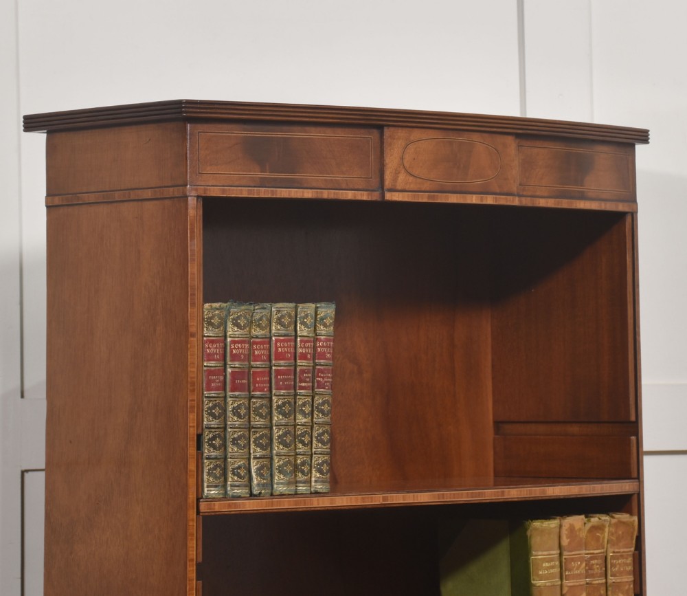 A tall, narrow mahogany open bookcase featuring five shelves, decorative inlay on the top frieze, and shaped bracket feet. View V