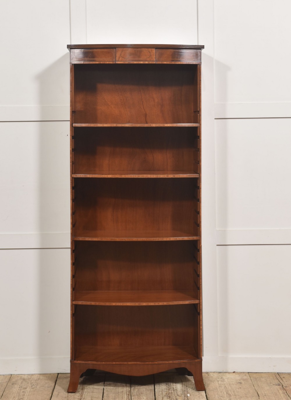 A tall, narrow mahogany open bookcase featuring five shelves, decorative inlay on the top frieze, and shaped bracket feet. View VI
