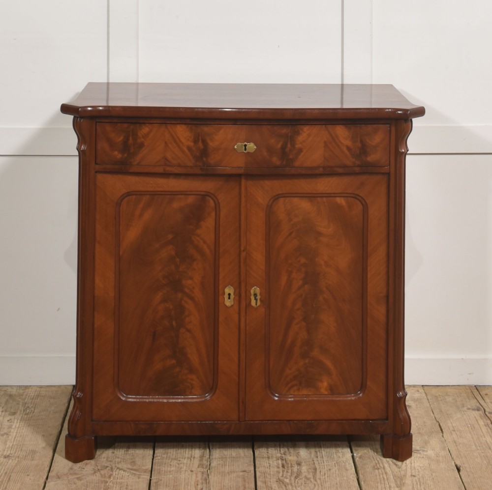 A 19th-century flame mahogany side cabinet with a single top drawer above two panelled cupboard doors with brass keyhole escutcheons. View II