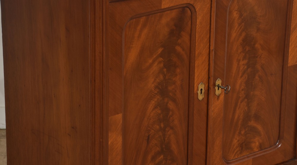 A 19th-century flame mahogany side cabinet with a single top drawer above two panelled cupboard doors with brass keyhole escutcheons. View VI