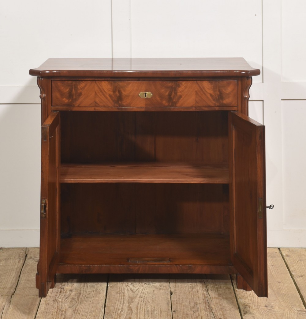 A 19th-century flame mahogany side cabinet with a single top drawer above two panelled cupboard doors with brass keyhole escutcheons. View XI