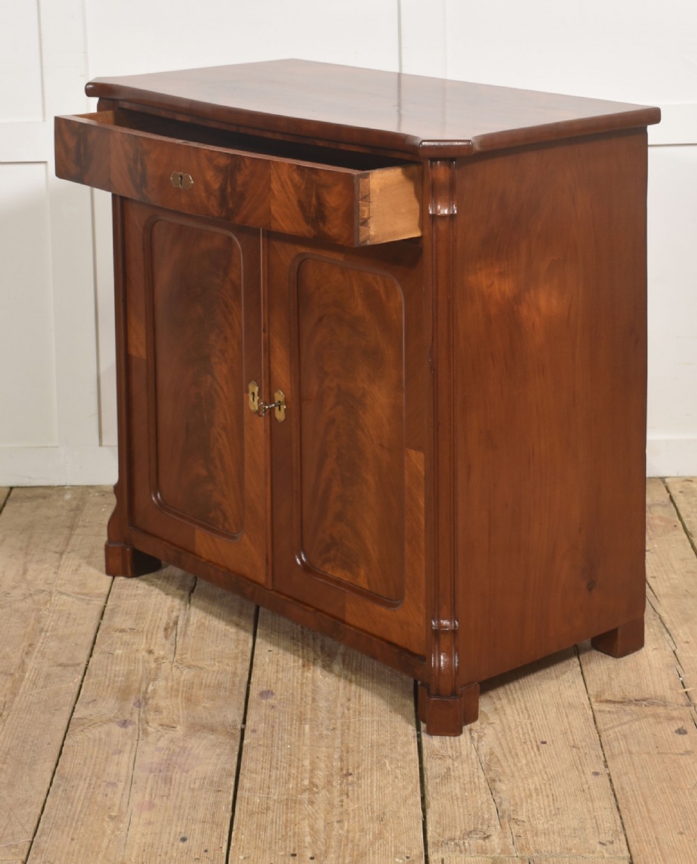 A 19th-century flame mahogany side cabinet with a single top drawer above two panelled cupboard doors with brass keyhole escutcheons. View XIII