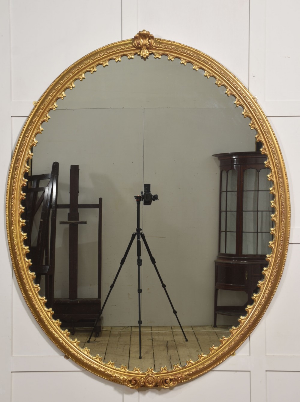 A large 19th-century oval wall mirror featuring a gilded frame with top shell cresting and scalloped inner detailing.