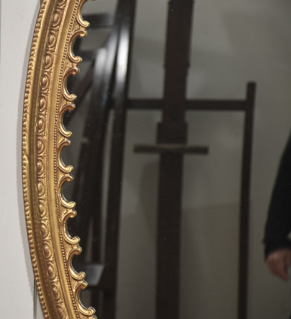 A large 19th-century oval wall mirror featuring a gilded frame with top shell cresting and scalloped inner detailing. View III