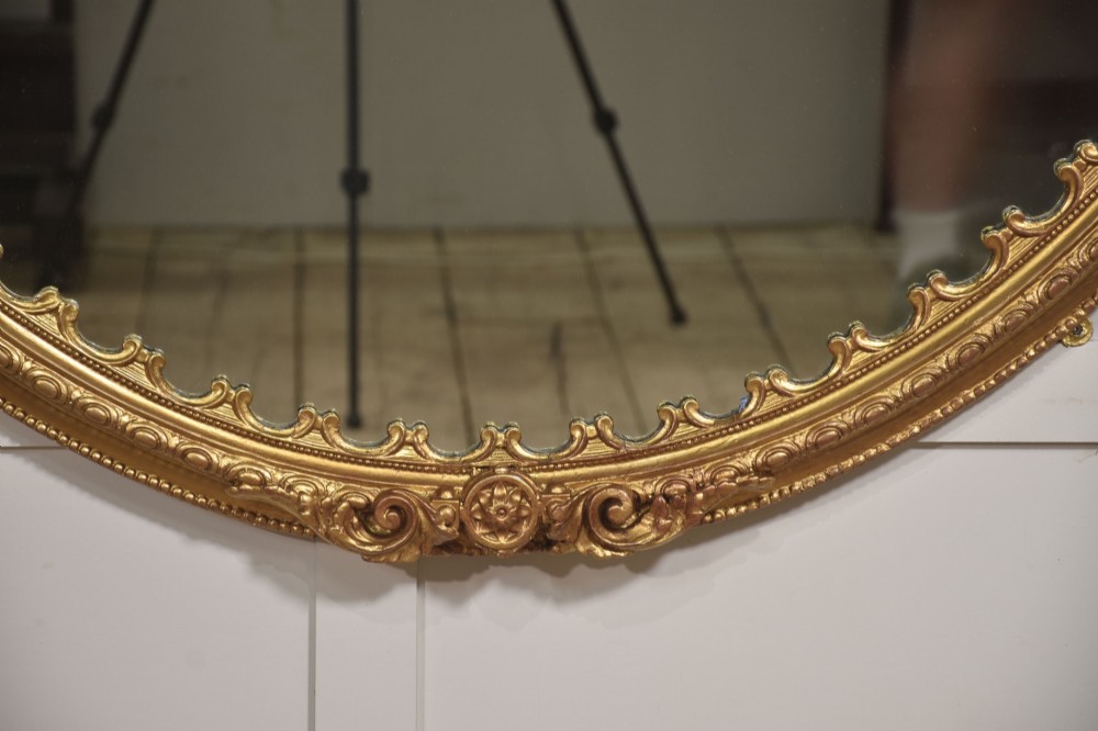 A large 19th-century oval wall mirror featuring a gilded frame with top shell cresting and scalloped inner detailing. View V