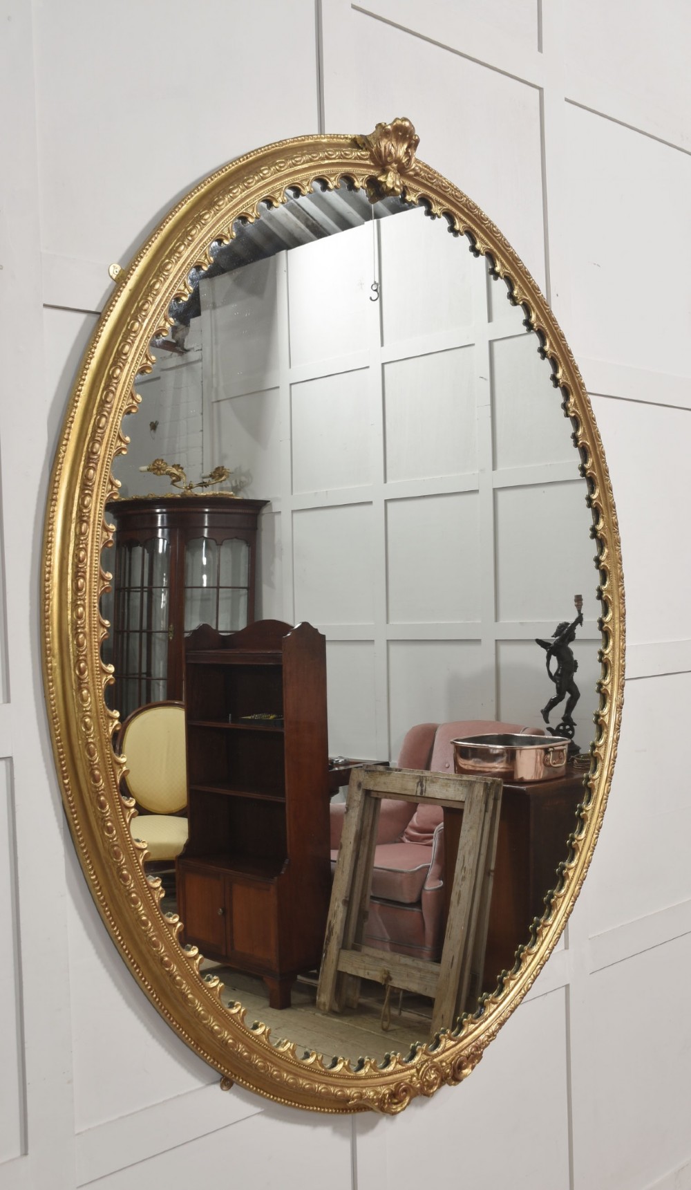 A large 19th-century oval wall mirror featuring a gilded frame with top shell cresting and scalloped inner detailing. View VI