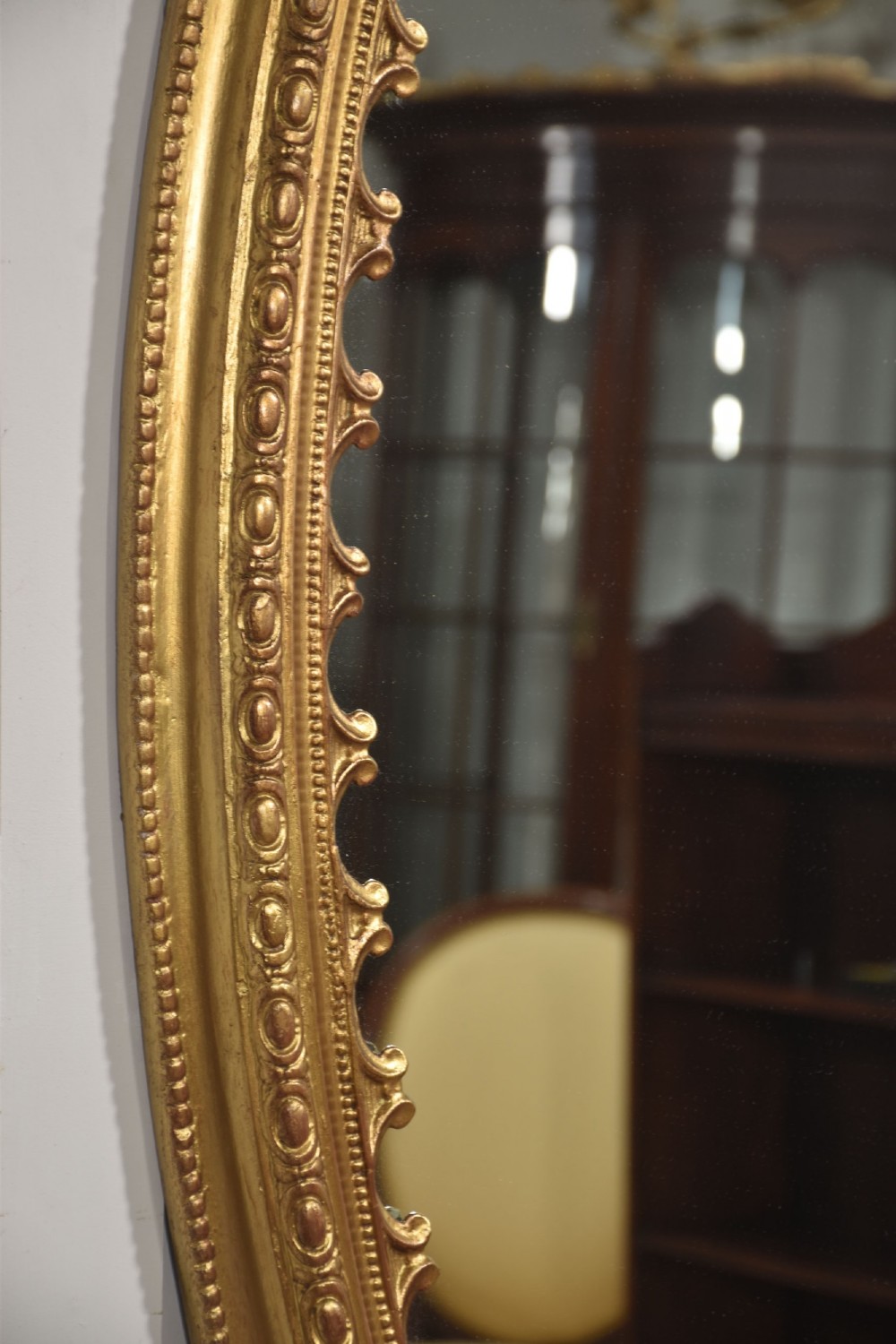 A large 19th-century oval wall mirror featuring a gilded frame with top shell cresting and scalloped inner detailing. View VIII