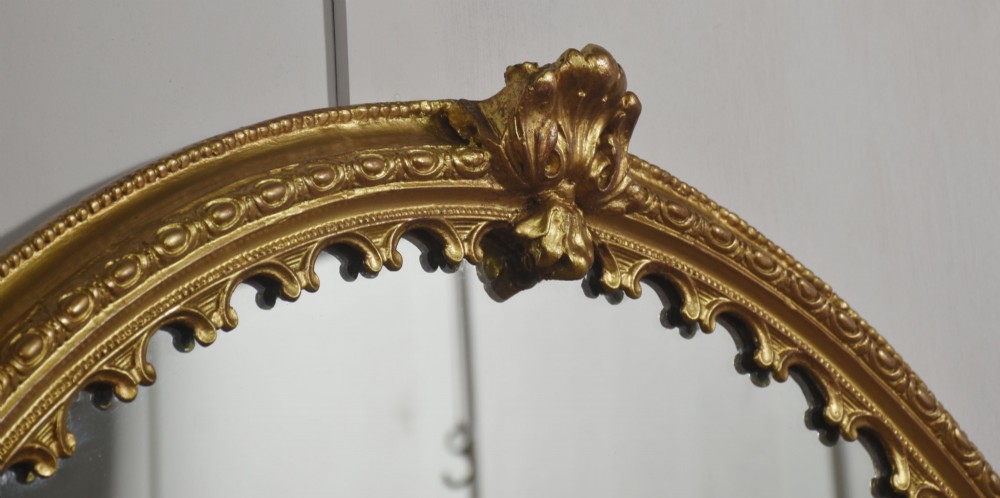 A large 19th-century oval wall mirror featuring a gilded frame with top shell cresting and scalloped inner detailing. View IX
