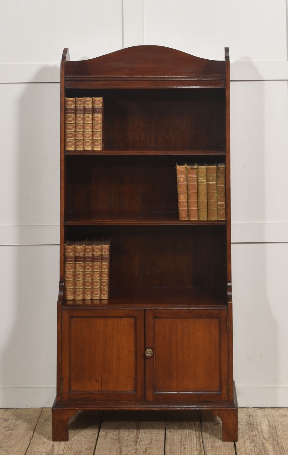 A tall Georgian style mahogany open bookcase featuring three open shelves, a contoured upper gallery, and a lower two-door panelled cupboard raised on bracket feet.