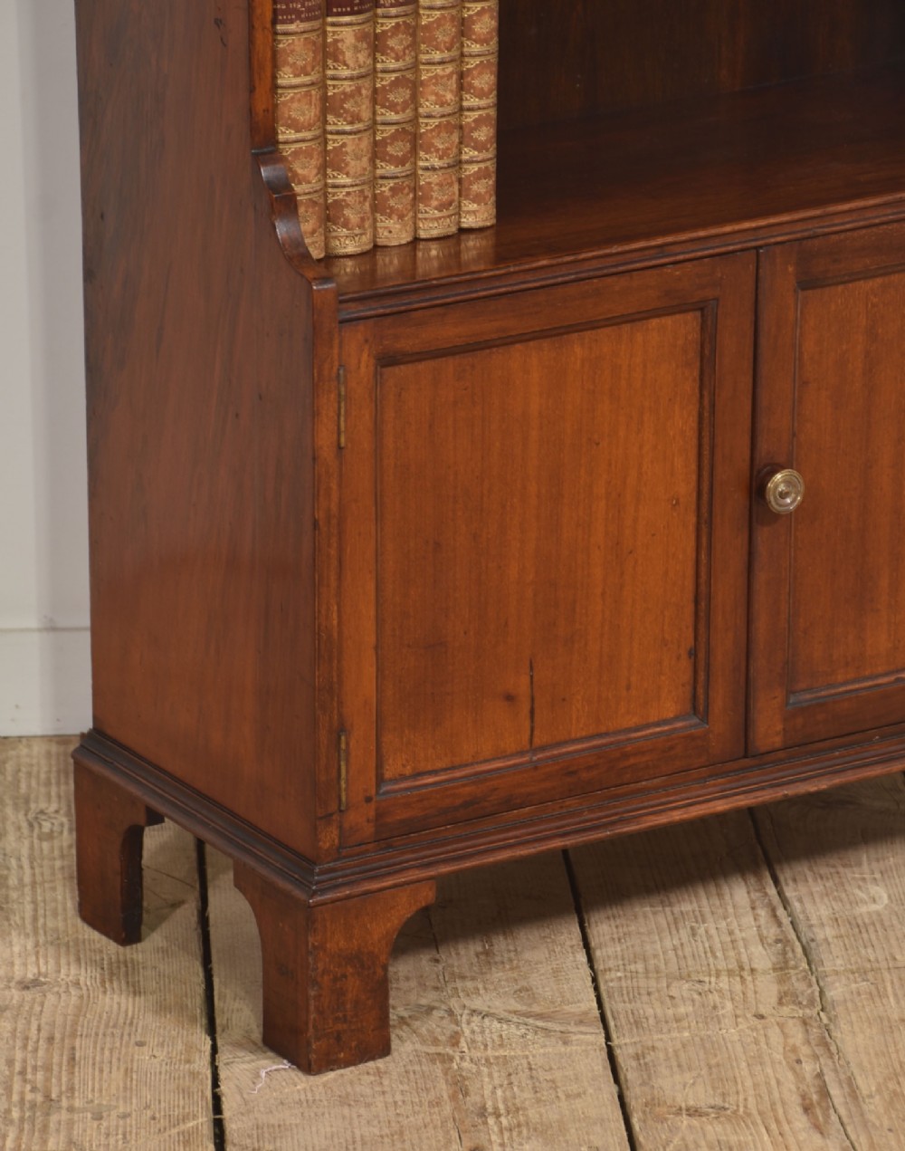 A tall Georgian style mahogany open bookcase featuring three open shelves, a contoured upper gallery, and a lower two-door panelled cupboard raised on bracket feet. View VI