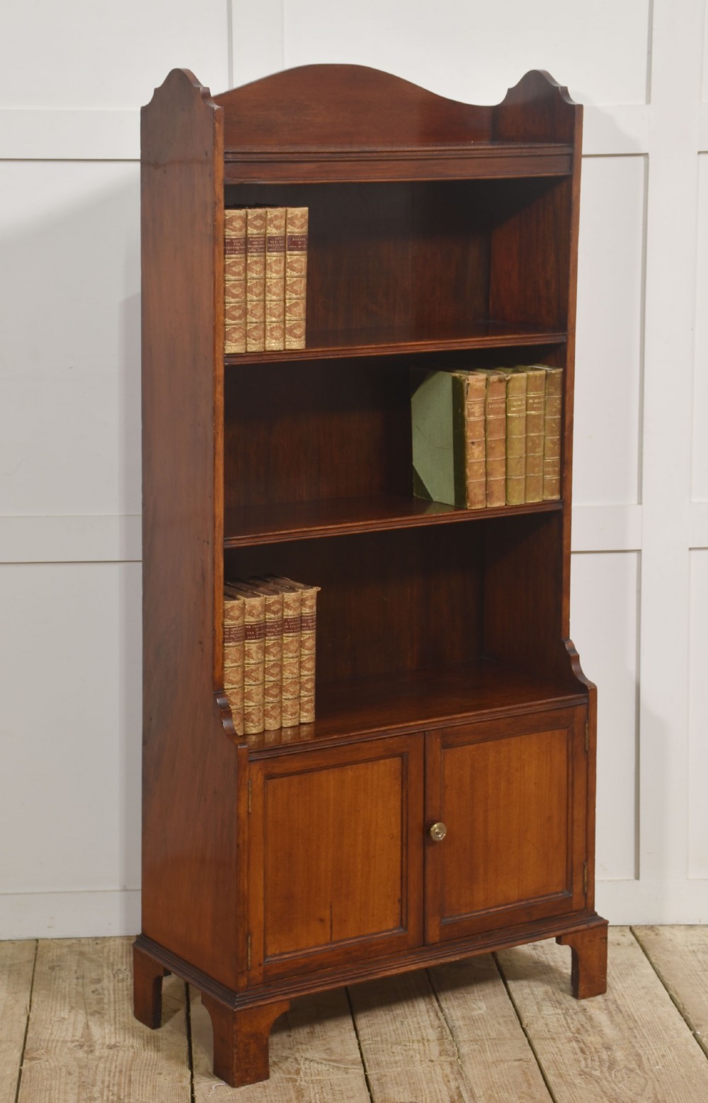 A tall Georgian style mahogany open bookcase featuring three open shelves, a contoured upper gallery, and a lower two-door panelled cupboard raised on bracket feet. View VII