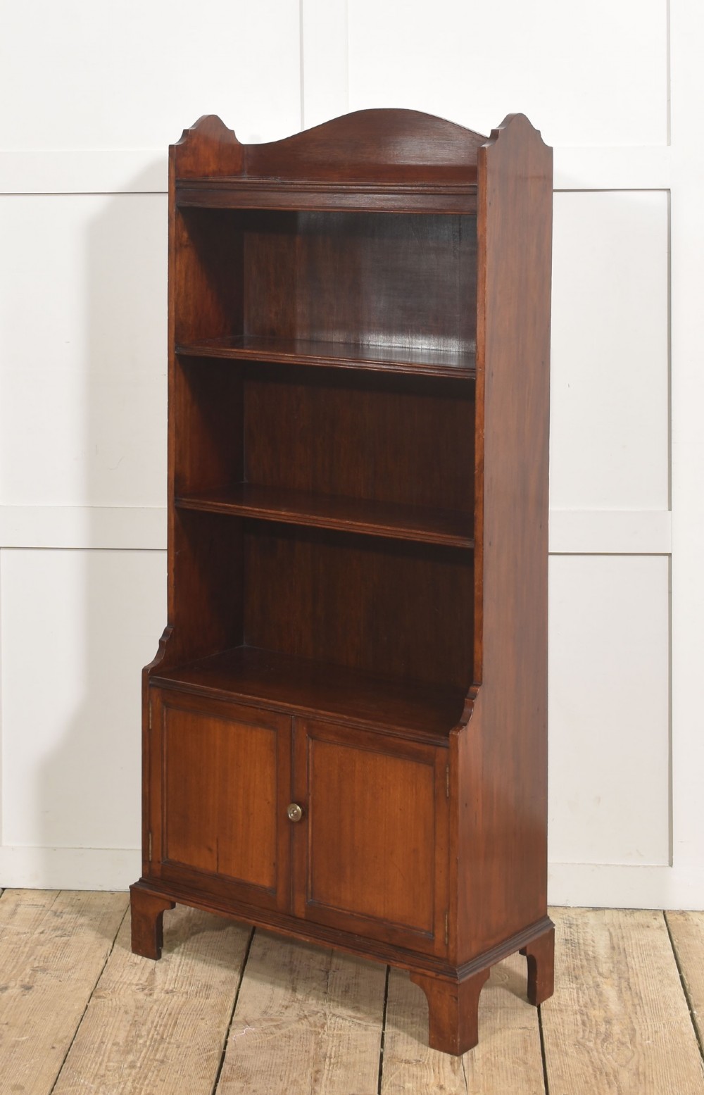 A tall Georgian style mahogany open bookcase featuring three open shelves, a contoured upper gallery, and a lower two-door panelled cupboard raised on bracket feet. View X