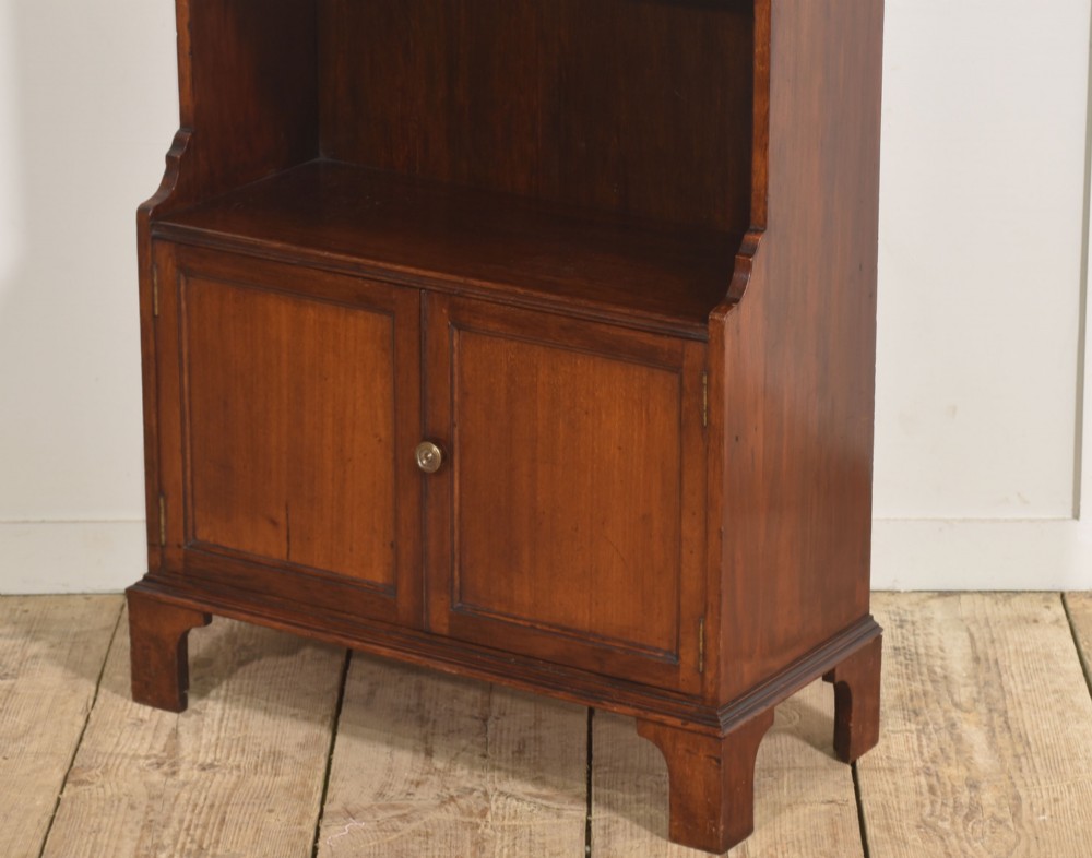 A tall Georgian style mahogany open bookcase featuring three open shelves, a contoured upper gallery, and a lower two-door panelled cupboard raised on bracket feet. View XI