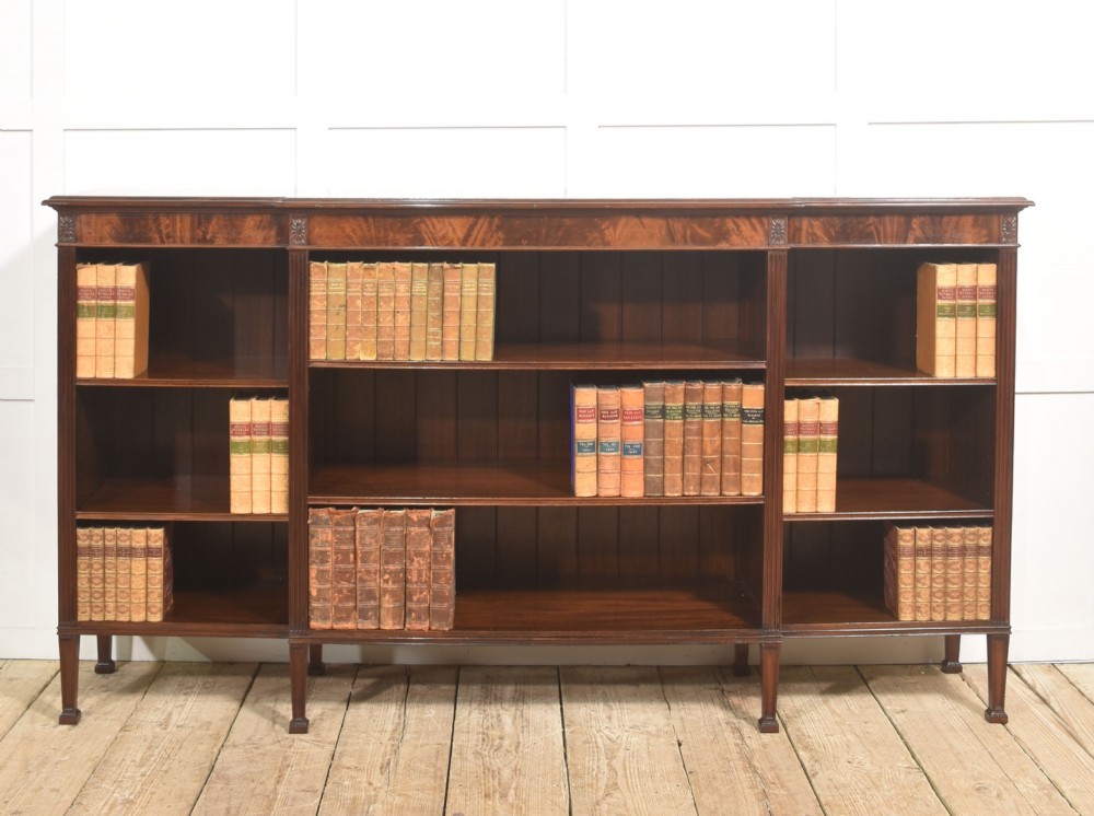 A low flame mahogany breakfront open bookcase featuring fluted pilasters, carved patera rosettes, and three open shelving sections.