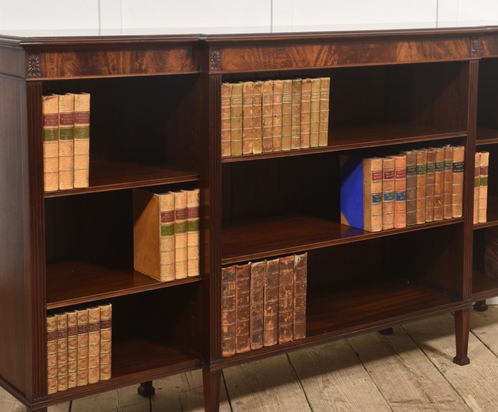 A low flame mahogany breakfront open bookcase featuring fluted pilasters, carved patera rosettes, and three open shelving sections. View V