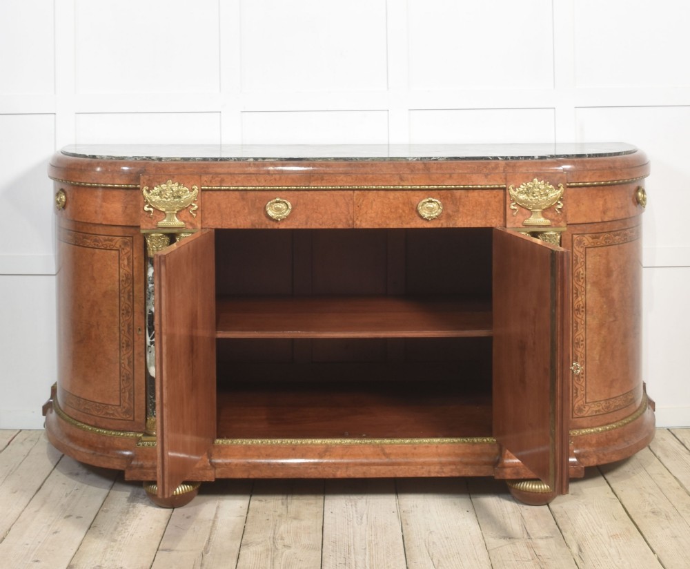 A French bow-front buffet sideboard featuring a dark marble top, burr walnut marquetry, central figural medallions, and flanking marble columns with gilt mounts. View VI