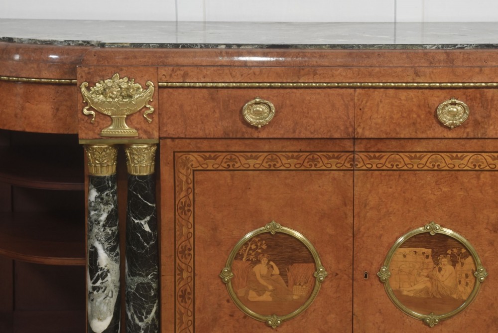 A French bow-front buffet sideboard featuring a dark marble top, burr walnut marquetry, central figural medallions, and flanking marble columns with gilt mounts. View X
