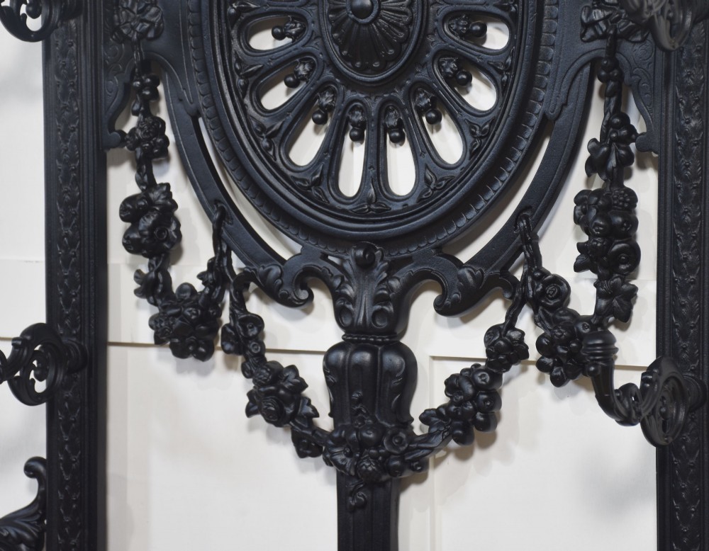 A tall black cast iron hall stand in the Coalbrookdale style featuring intricate scrollwork, coat hooks, an umbrella rail, and a drip tray base. View VIII
