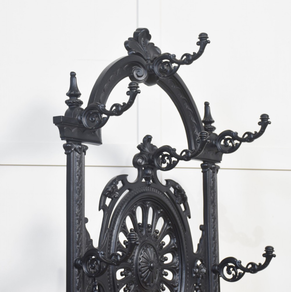 A tall black cast iron hall stand in the Coalbrookdale style featuring intricate scrollwork, coat hooks, an umbrella rail, and a drip tray base. View X