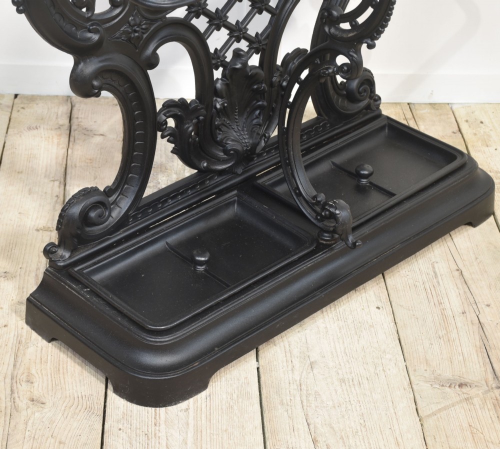 A tall black cast iron hall stand in the Coalbrookdale style featuring intricate scrollwork, coat hooks, an umbrella rail, and a drip tray base. View XII