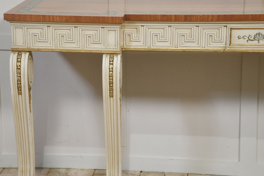 A long Neoclassical style console table featuring a polished timber top with an inlaid border, an off-white apron decorated with a painted Greek key pattern, and carved scroll legs with gilt detailing. View VII