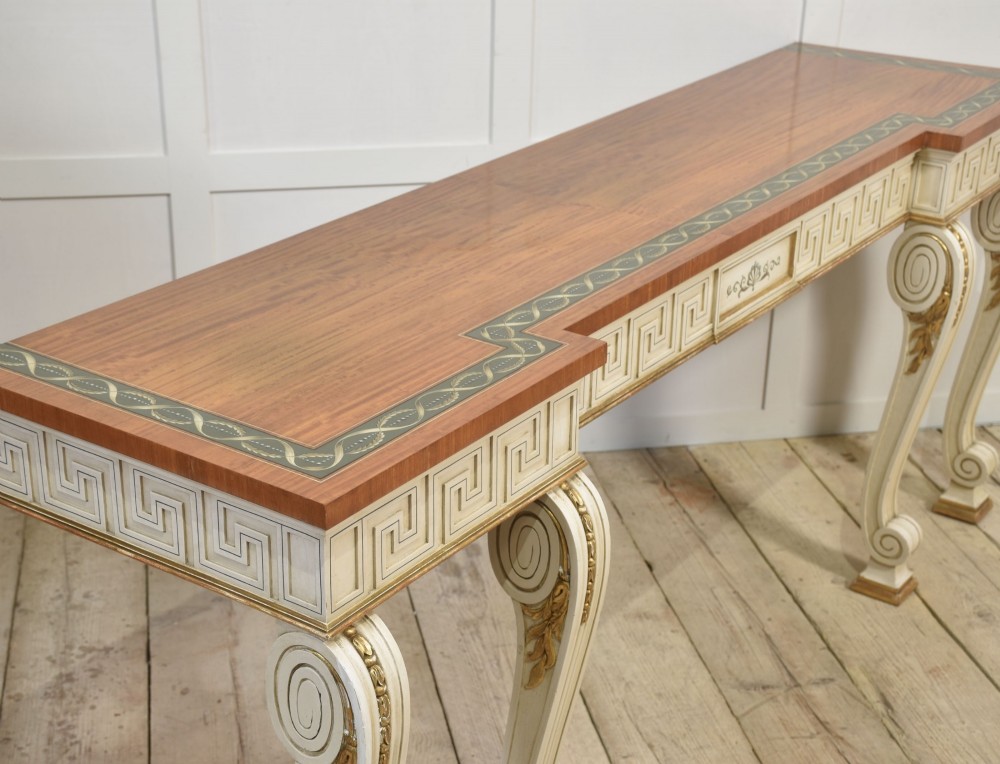 A long Neoclassical style console table featuring a polished timber top with an inlaid border, an off-white apron decorated with a painted Greek key pattern, and carved scroll legs with gilt detailing. View X