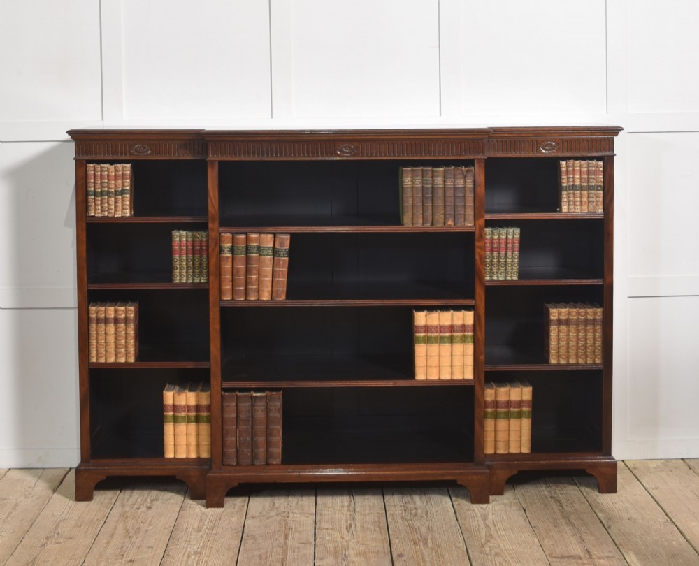 A large mahogany breakfront open library bookcase featuring multiple shelves, a fluted frieze with carved medallions, and sturdy bracket feet.