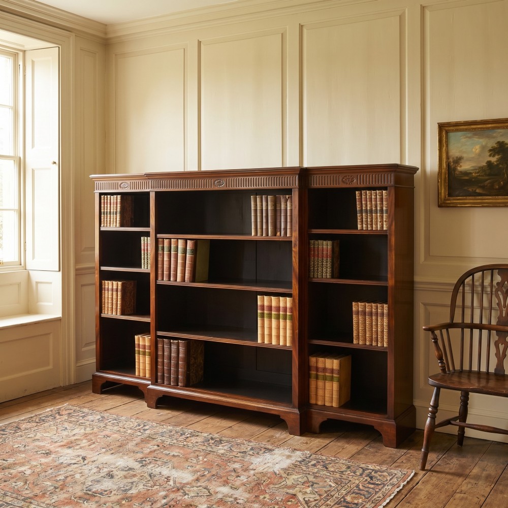 A large mahogany breakfront open library bookcase featuring multiple shelves, a fluted frieze with carved medallions, and sturdy bracket feet. View VII