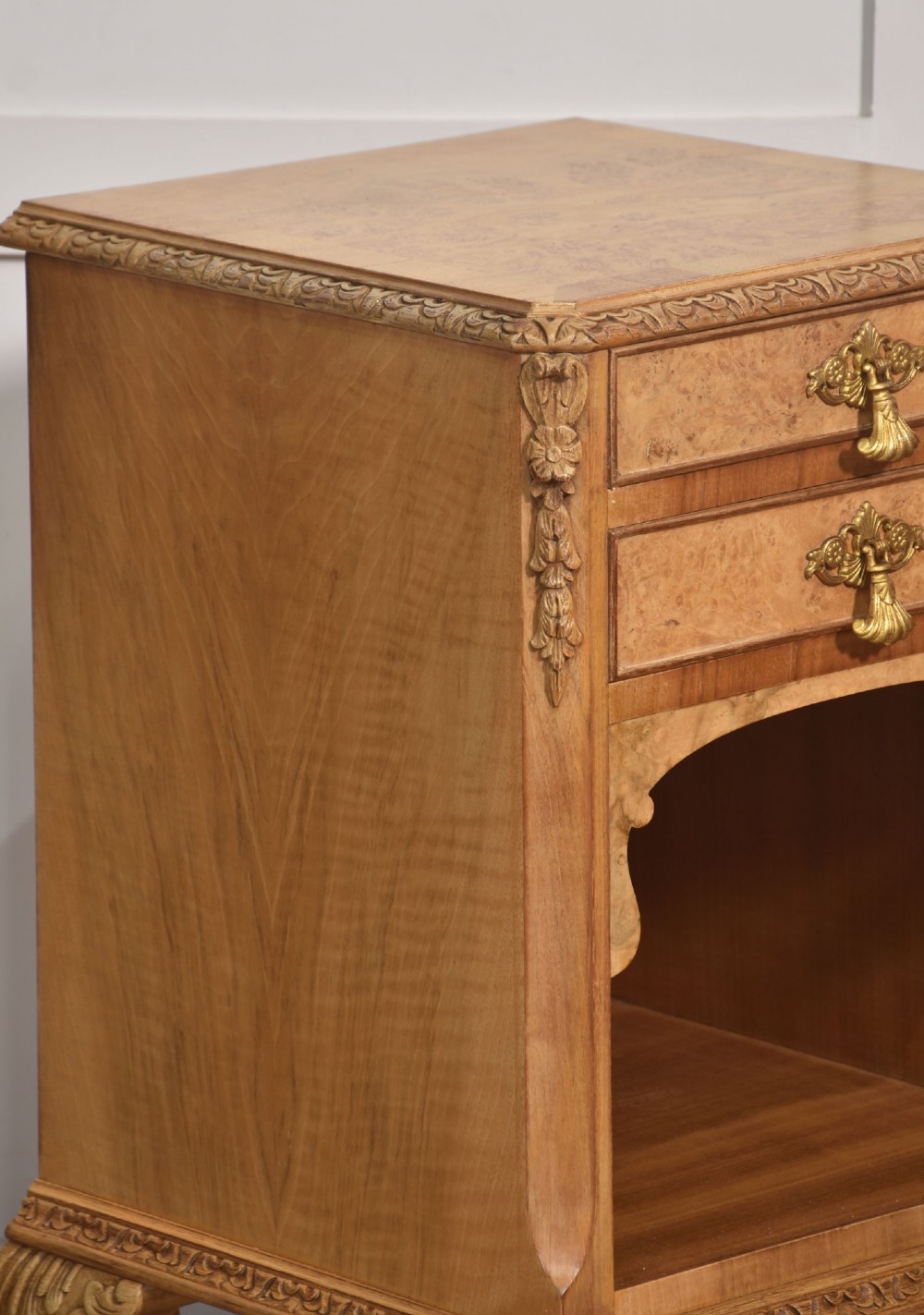 A pair of golden burr walnut bedside cabinets featuring two upper drawers with brass drop handles above an open cubby, set on carved cabriole legs with claw and ball feet. View IV